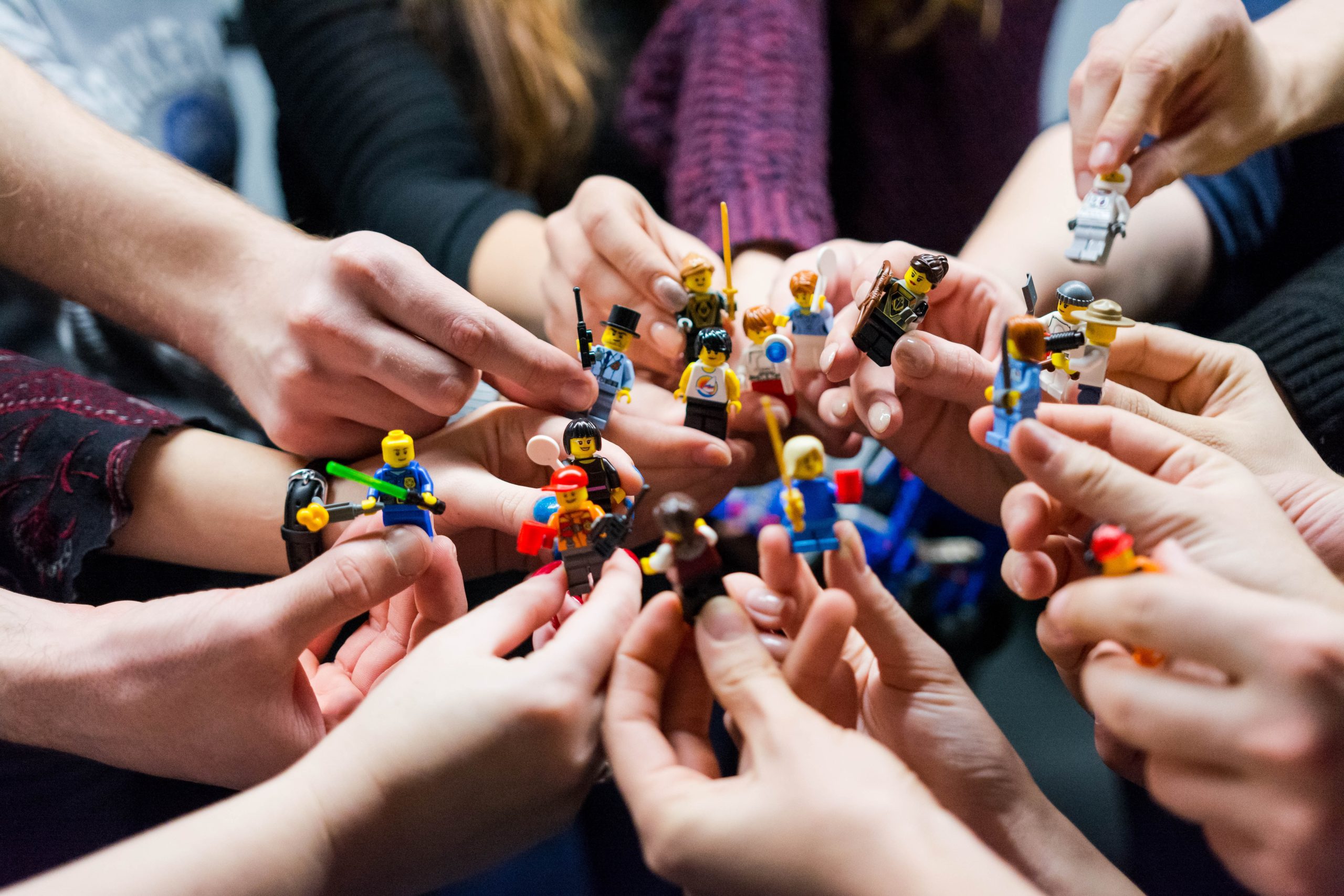 Mehrere Hände halten verschiedene Lego-Figuren zueinander und bilden einen Kreis.